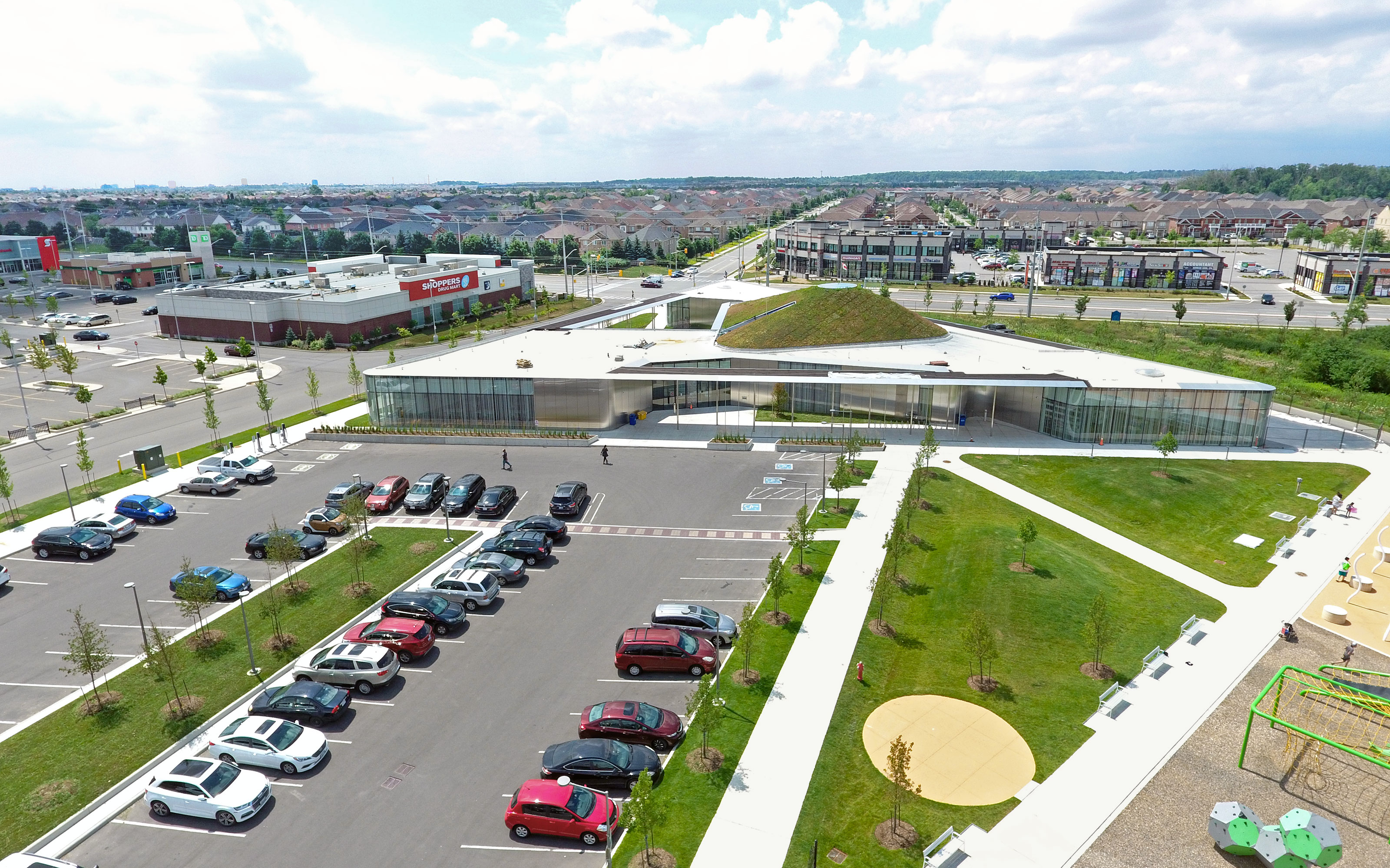 The triangular building with its green roof dome is impressive from aerial view. Large parking area in front of a building with pitched green roof